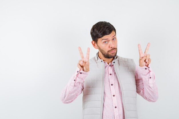 Homme mûr montrant un geste de paix en chemise, veste sans manches et à la réflexion. vue de face.