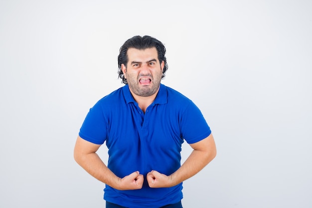 Homme mûr montrant les muscles en t-shirt bleu, jeans et à la colère. vue de face.