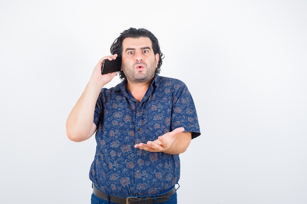 Homme mûr parlant au téléphone mobile en chemise et à la perplexité, vue de face.