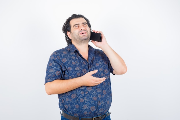 Homme mûr parlant au téléphone mobile en chemise et à la vue de face, heureux.
