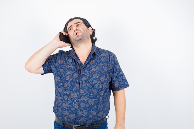 Homme mûr parlant au téléphone mobile en chemise et à la vue mécontent, de face.