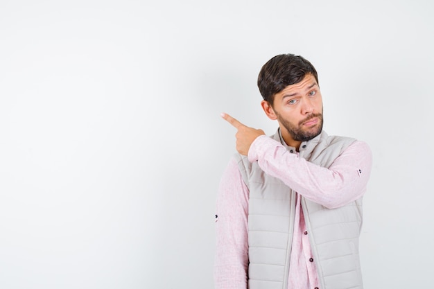 Homme mûr pointant vers le coin supérieur gauche en chemise, veste sans manches et pensif , vue de face.