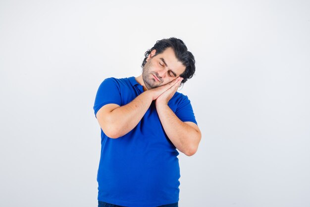 Homme mûr s'appuyant sur les paumes comme oreiller en t-shirt bleu et à la vue de face, somnolent.