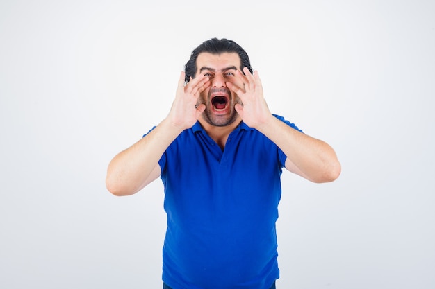 Homme mûr se tenant la main près de la bouche comme appelant quelqu'un en t-shirt bleu