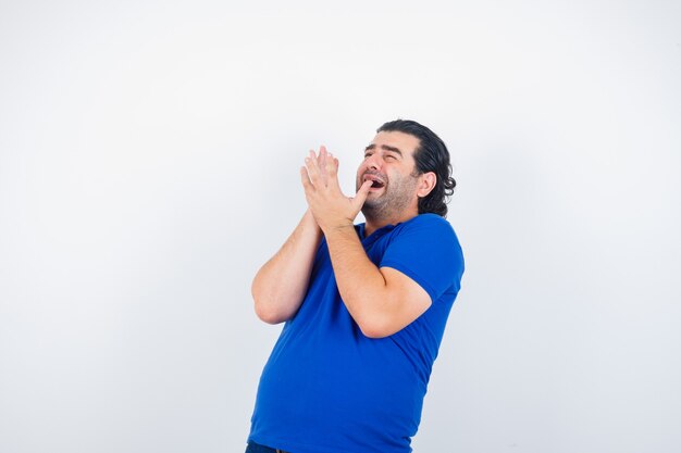 Homme mûr en t-shirt bleu, jeans levant les mains de manières effrayées et à la peur, vue de face.