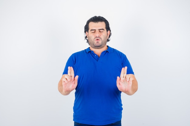 Homme Mûr En T-shirt Bleu, Jeans Montrant Le Geste De L'argent Et à La Vue Calme, De Face.