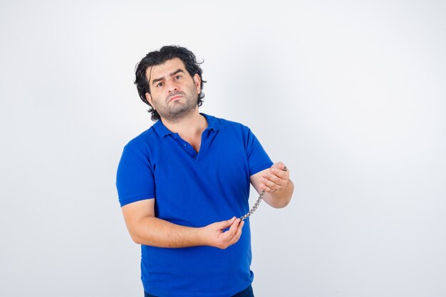 Homme mûr en t-shirt bleu tenant la chaîne et à la perplexité, vue de face.