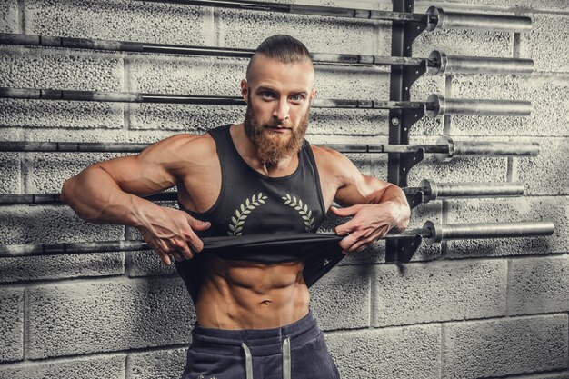 Homme musclé barbu dans un t-shirt gris posant dans un club de gym.