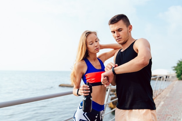 Homme musclé beau et fille sportive vérifiant un moment sur les montres intelligentes