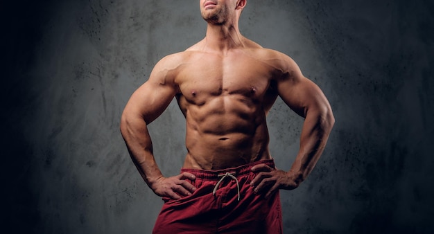Un homme musclé avec de belles muscules pose pour le photographe dans un studio photo sombre.