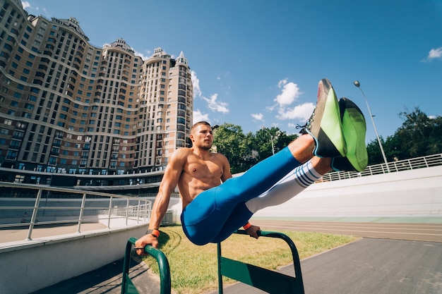 Homme musclé fort faisant des exercices sur des barres asymétriques dans une salle de sport de rue en plein air