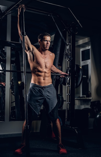 Homme musclé torse nu athlétique posant avec des haltères dans un club de gym.