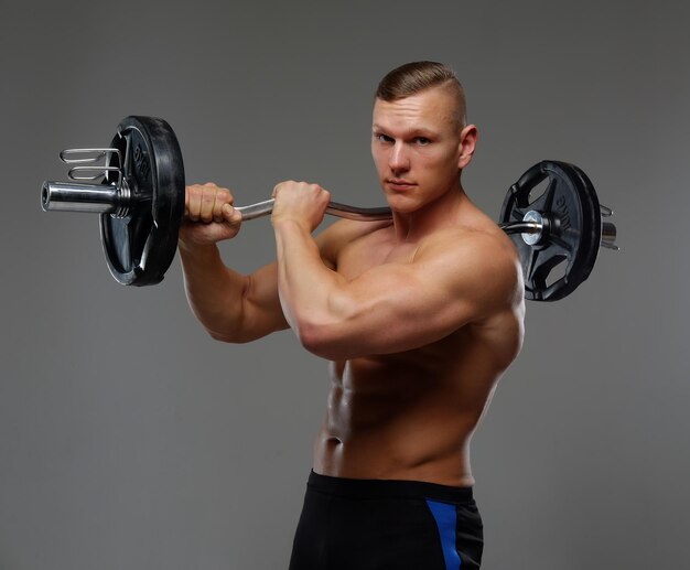 L'homme musclé torse nu tient la barre. Isolé sur un fond gris.