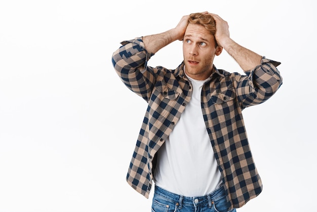 Homme Nerveux Aux Cheveux Roux Tenant Les Mains Sur La Tête Regardant De Côté La Publicité Et Paniqué Se Sentant Inquiet D'avoir Un Problème Alarmé Debout Sur Fond Blanc