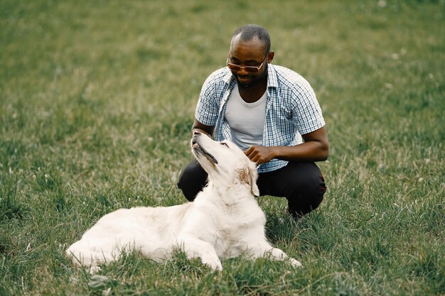 Homme noir américain assis sur une herbe avec son chien. Homme portant un t-shirt blanc et une chemise à carreaux bleue