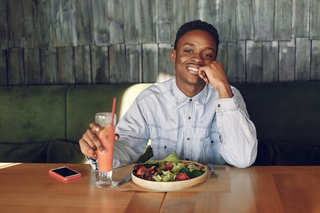 Photo gratuite homme noir assis dans un café et manger une salade de légumes