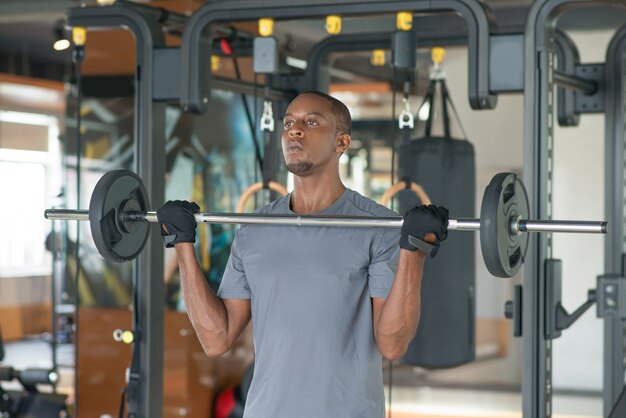 Homme noir debout et soulever une barre dans la salle de gym