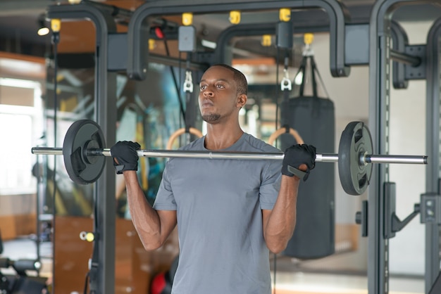 Homme noir debout et soulever une barre dans la salle de gym