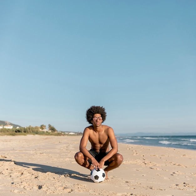Homme noir décontracté avec ballon sur la plage