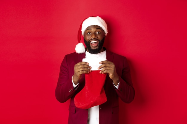 Homme noir excité chaussette de Noël ouverte avec des cadeaux et des bonbons