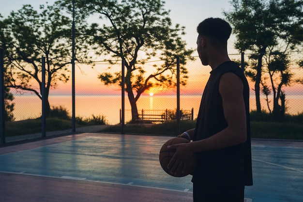 Photo gratuite homme noir, faire du sport, jouer au basket au lever du soleil, silhouette