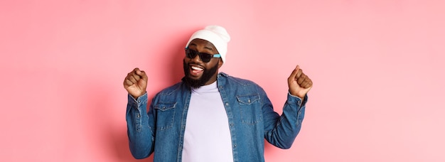 Homme noir heureux et insouciant célébrant la danse et s'amusant portant un bonnet et des lunettes de soleil standi