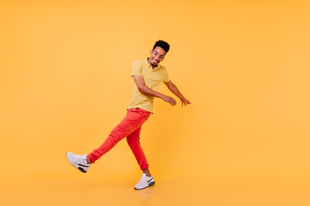 Homme noir inspiré dans la danse drôle de tenue décontractée lumineuse. Modèle masculin africain en riant en t-shirt jaune et pantalon rouge s'amuser.