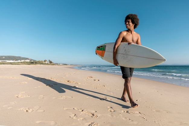 Homme noir marchant le long de la plage avec planche de surf