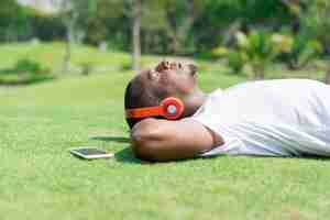 Photo gratuite homme noir serein se reposer dans le parc et écouter de la musique.