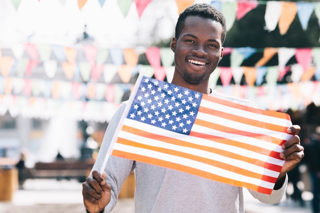 Homme noir souriant tenant le drapeau américain et regardant la caméra