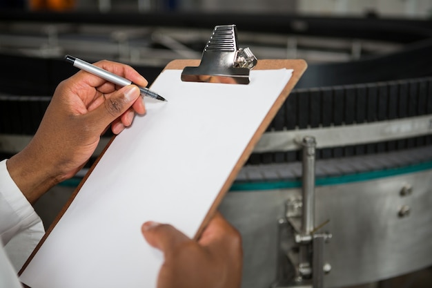 Homme notant sur le presse-papiers à l'usine de jus