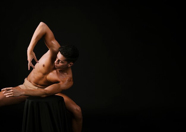 Homme nu se penchant avec le coude sur une chaise et levant la main