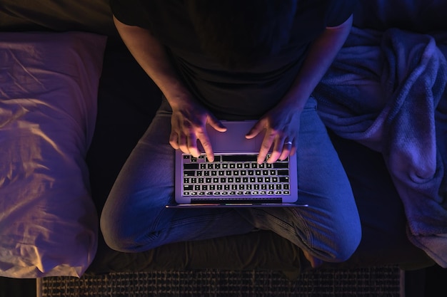 Un homme occupé à travailler sur un ordinateur portable tard dans la nuit, à taper des textes, à faire des heures supplémentaires.