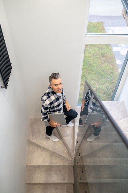 Homme avec ordinateur portable monter les escaliers en regardant la caméra