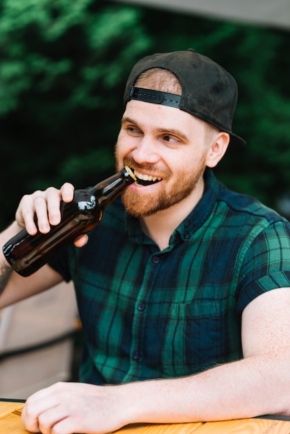 Homme ouvrant le bouchon de la bouteille de bière avec ses dents