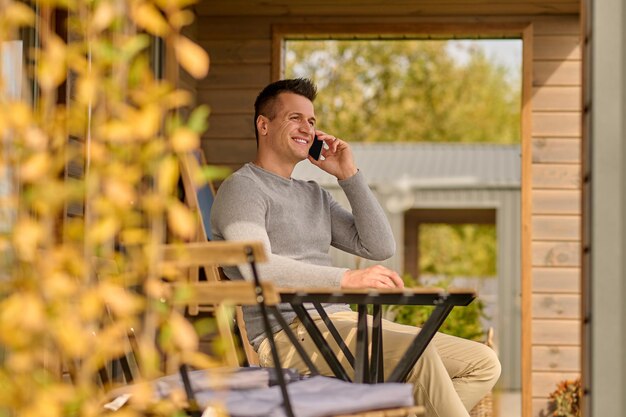 Homme parlant sur smartphone assis sur une terrasse ouverte