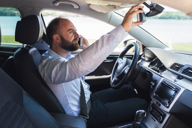 Homme parlant sur téléphone mobile en ajustant le rétroviseur de la voiture