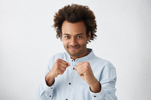 Photo gratuite homme à la peau sombre confiant avec une coiffure africaine en chemise formelle blanche tenant les poings devant lui