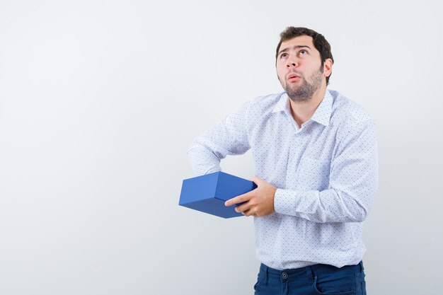 L'homme pensant tient une boîte-cadeau sur fond blanc