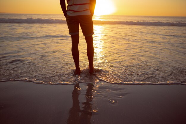 Homme pensif debout avec les mains dans les poches sur la plage