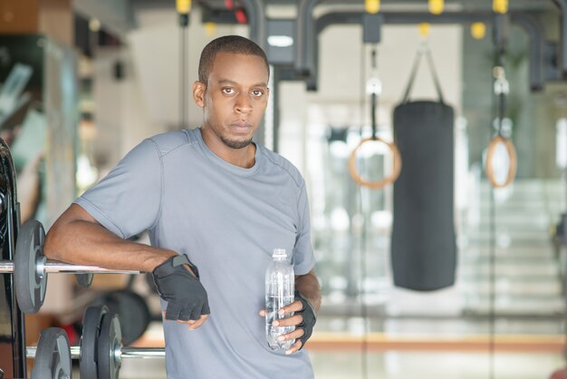 Homme pensif tenant une bouteille d&#39;eau, debout dans une salle de sport