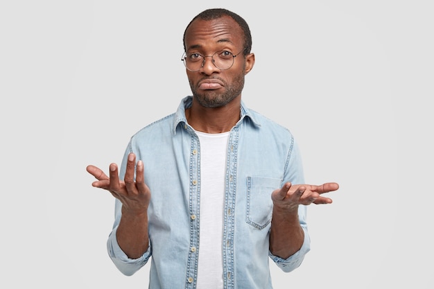 Photo gratuite un homme perplexe regarde avec une expression désemparée, semble douteux, ne peut pas prendre de décision, vêtu de vêtements décontractés, isolé sur un mur blanc