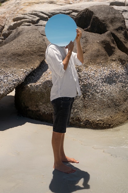 Homme à la plage posant avec un miroir réfléchissant rond