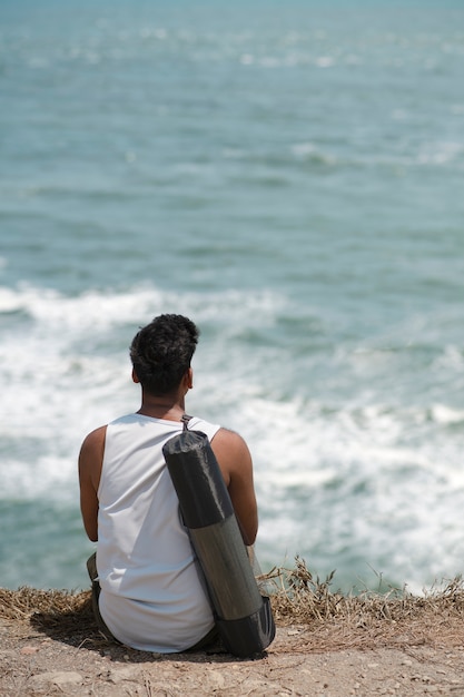 Photo gratuite homme plein coup assis avec un tapis de yoga