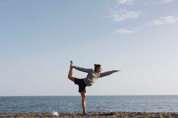 Photo gratuite homme plein coup faisant du yoga sur la plage