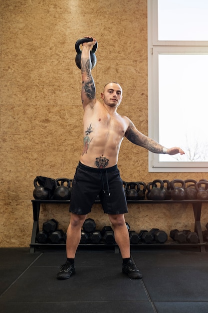 Photo gratuite homme plein coup faisant de l'exercice avec kettlebell à l'intérieur