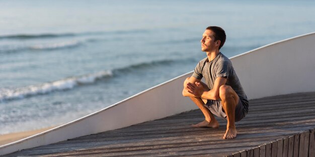 Homme plein coup faisant la guirlande pose à l'extérieur près de la mer