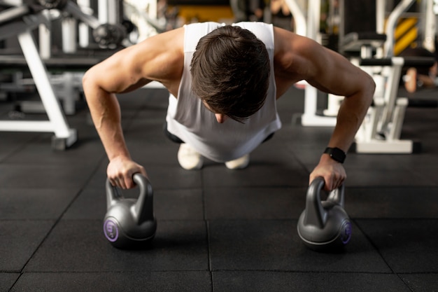 Photo gratuite homme plein coup s'entraînant avec des kettlebells au gymnase