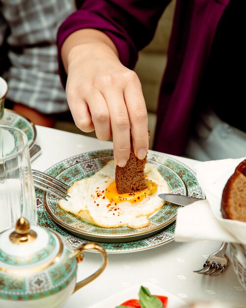 Homme plongeant un pain dans un œuf au plat servi pour le petit déjeuner