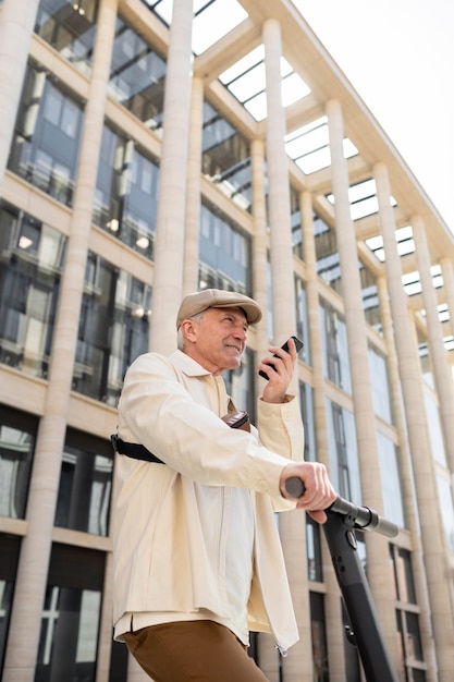 Homme plus âgé dans la ville avec un scooter électrique utilisant un smartphone